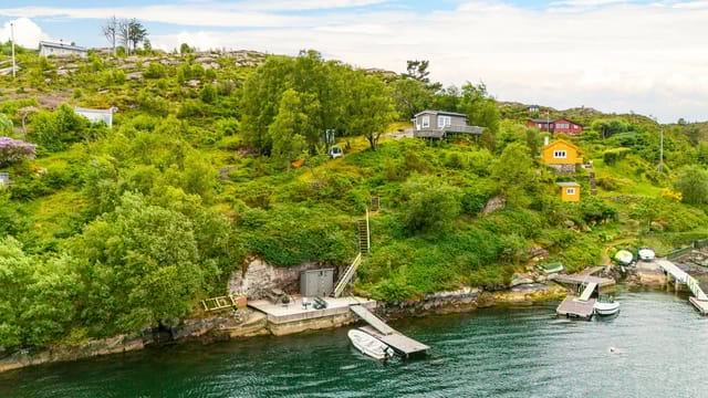 The property is located in hilly terrain with lush vegetation and direct access to the sea via a dock and private boat. The cabin is situated high in the terrain with views over the water.