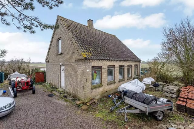 An old brick house with a sloped roof in a rural setting.