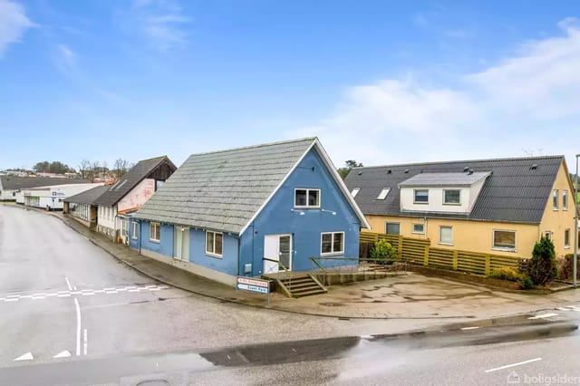 A blue house on a corner with a small staircase leading to the front door.