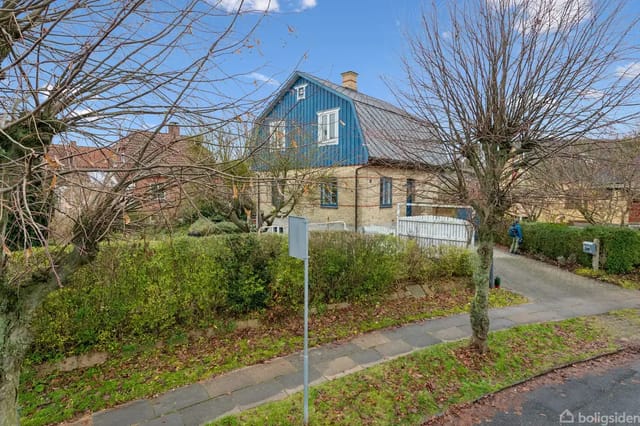 House with blue gable and brown facade in a villa garden surrounded by trees and bushes.
