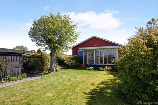 Red house with large windows in a well-maintained garden with green lawn and trees.