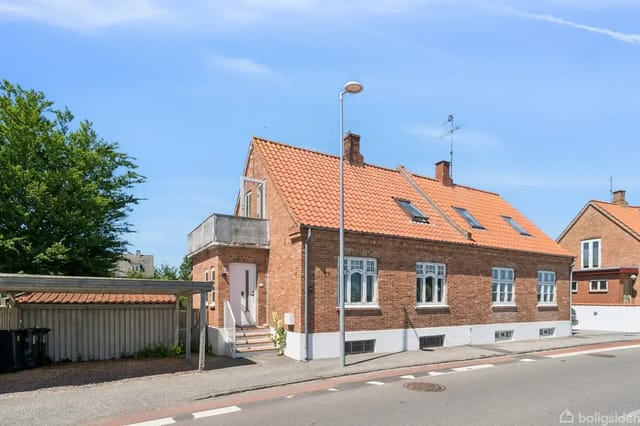 Red brick house with orange tiled roof, two stories, small entrance steps, and carport to the left.