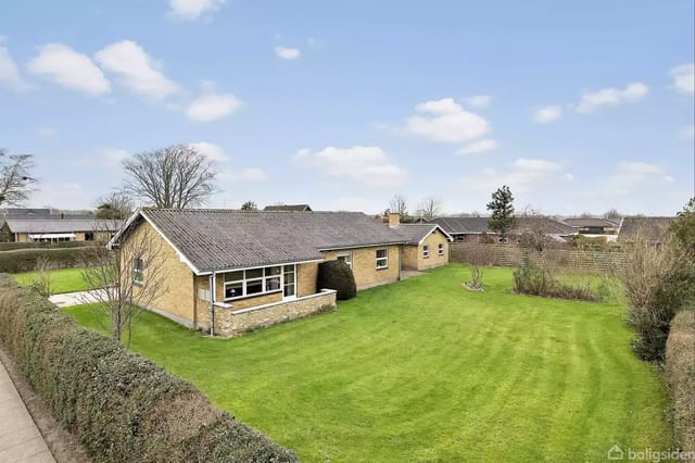 A yellow brick house on a well-maintained lawn with bushes around, located in a residential area under a blue sky with clouds.