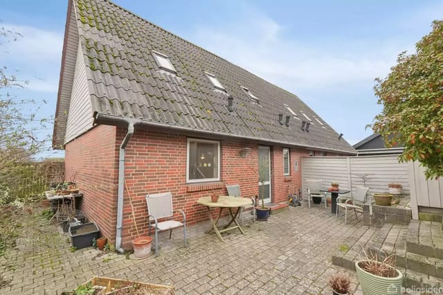 A brick house with a sloped roof and a small terrace with tables and chairs.