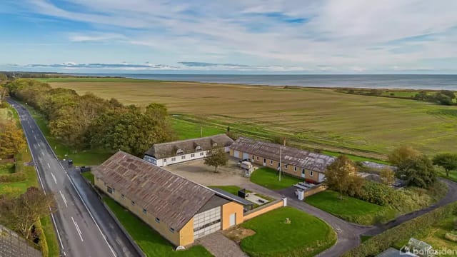 Aerial view of farm buildings surrounded by fields with sea view in the background.