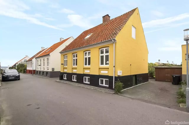 Yellow houses on a quiet street with a parked car and red roofs.