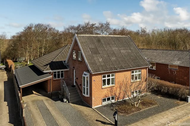 Front view of the villa with red brick, black tile roof, raised wooden terrace, and lawn