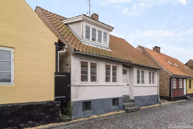 A charming older house with a white facade and red tile roof along a cobblestone street.