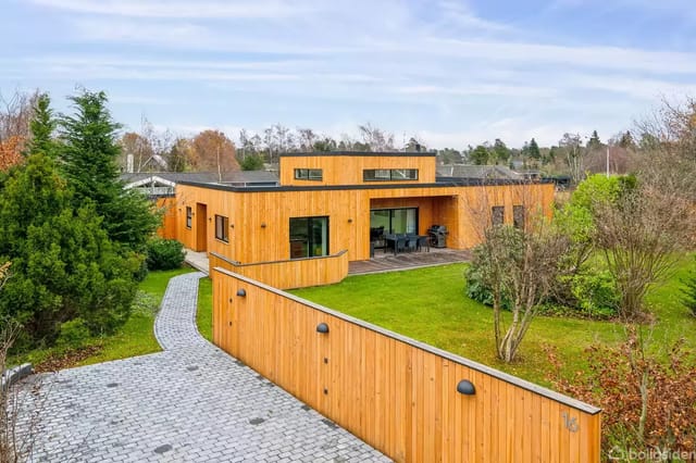 A modern wooden house surrounded by a lush garden.