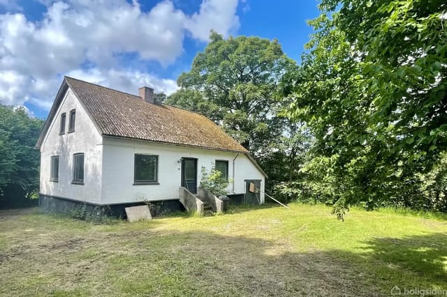 House on a grassy plot with steps to the main entrance, surrounded by trees under a partly cloudy sky.
