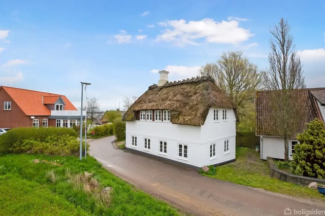White thatched house in rural surroundings with grass and trees under a blue sky.