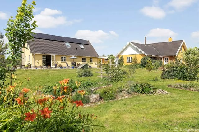 Two yellow houses side by side in a lush garden with blooming orange lilies and a well-kept lawn under a blue sky with light clouds.